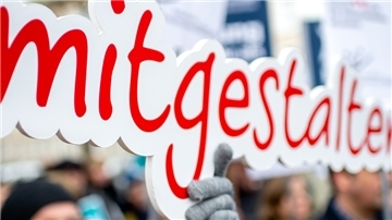 Ein Mann hält ein Schild mit dem Schriftzug mitgestalten in die Höhe.