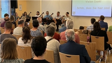 Ein Gitarrenensemble spielt vor Publikum auf Holzstühlen.