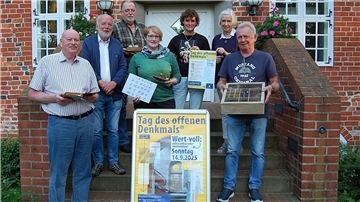 Mehrere Menschen stehen vor einem Gebäude und halten historische Gegenstände und Plakate in der Hand. 