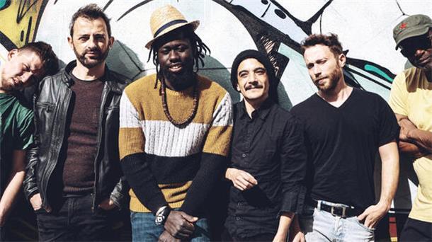 Die sechs Musiker der Band Afrodream stehen lässig vor einer bunt bemalten Wand und lächeln in die Kamera.