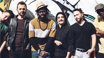 Die sechs Musiker der Band Afrodream stehen lässig vor einer bunt bemalten Wand und lächeln in die Kamera.