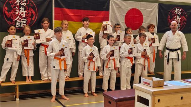 Junge Karateka halten ihre Urkunden zur Gürtelprüfung in die Höhe.