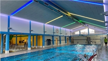 Ein Sportschwimmbecken mit einer neuen grauen Schallschutzdecke und blauen, gelben und grünen Leuchtstoffröhren.