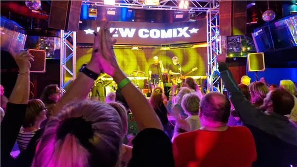 Eine Bühne mit einer Band, davor tanzende und klatschende Fans.