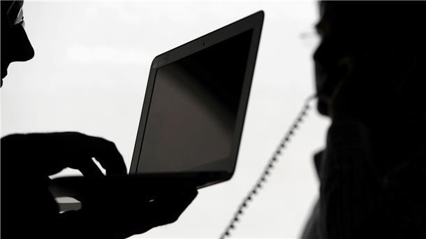 Zwei Männer stehen mit Computer und Telefon vor einem Fenster. Das Bild symbolisiert das Thema Telefonüberwachung.