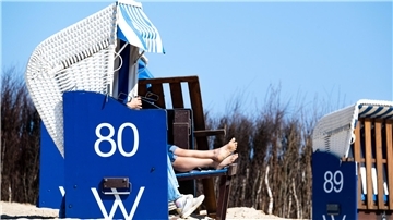 Menschen sitzen in einem Strandkorb am Strand.