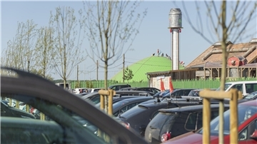 Parkplatz vor einem Freizeitpark. Im Hintergrund spielen Kinder auf einer Hüpfburg.