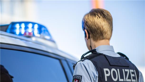 Eine Polizistin steht vor einem Streifenwagen, dessen Blaulicht leuchtet.