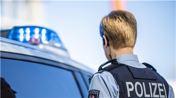 Eine Polizistin steht vor einem Streifenwagen, dessen Blaulicht leuchtet.
