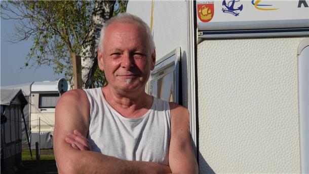 Ein Mann steht im Unterhemd angelehnt an seinem Camper.