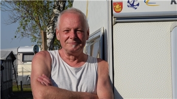 Ein Mann steht im Unterhemd angelehnt an seinem Camper.