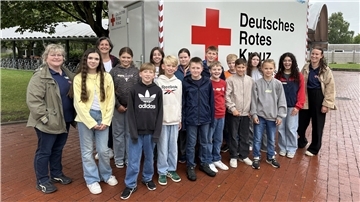 Gruppe von Schülerinnen und Schülern sowie Betreuenden steht vor einem Anhänger des Deutschen Roten Kreuzes beim LifeGRID-Projekt am Gymnasium Brake.