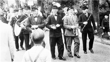 Ein Umzug mit Musikern bewegt sich auf einer Dorfstraße.