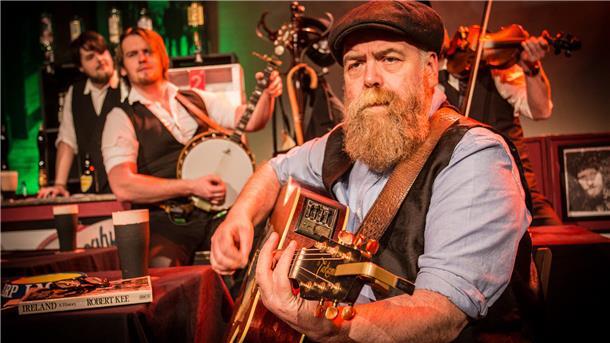 Ein bärtiger Mann mit Gitarre. Das Foto zeigt eine Szene aus der Show „Seven drunken Nights".