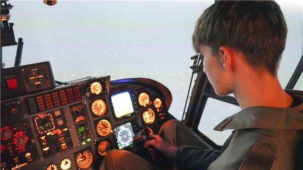 Ein Jugendlicher sitzt in einem realistisch beleuchteten Hubschrauber-Simulator und bedient das Steuer. Vor ihm befinden sich zahlreiche beleuchtete Anzeigen und Instrumente.