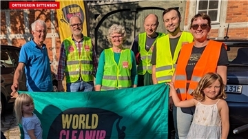 Einige Männer, Frauen und Kinder stehen nebeneinander und halten ein Transparent zum „World Cleanup Day“