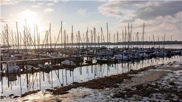 Die Sonne scheint auf einen Bootshafen an der Kieler Förde, aus dem das Sturmtief „Poly“ das Wasser herausgedrückt hat, so dass die normalerweise mit Wasser bedeckten Ufer trocken liegen.