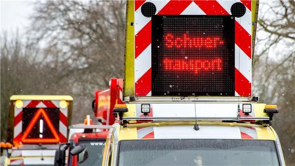 Auto mit Hinweistafel „Schwertransport“ auf dem Dach. 