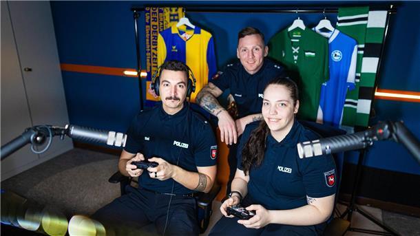 Die Streamer „Sini“, „Janni“ und „Jo“ sitzen vor dem Niedersachsen-Derby vor Trikots von Eintracht Braunschweig und Hannover 96 im Polizeistudio.