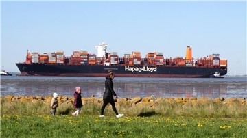 Die Tihama wird von Schleppern auf der Weser begleitet. Spaziergänger laufen am Ufer entlang. 