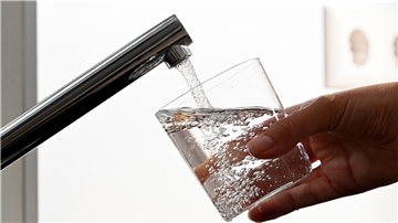 Hand mit einem Glas unter unter einem Wasserhahn
