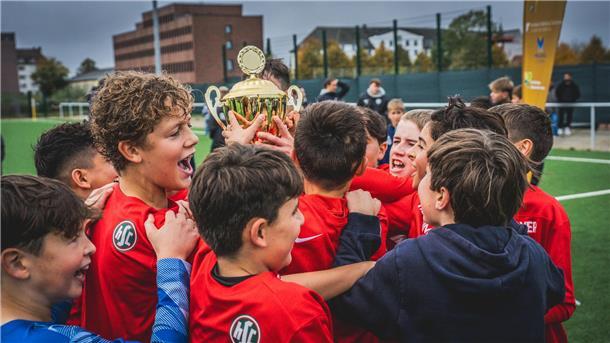 Jugendfußballer zeigen ihre Emotionen nach einem gewonnenen Spiel und halten einen Pokal in die Höhe.  