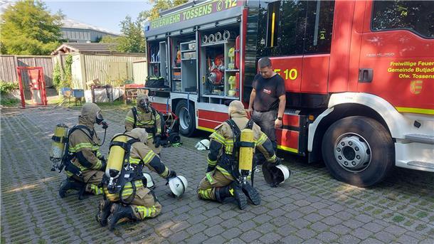 Feuerwehr in voller Montur knien vor einem Feuerwehrauto.