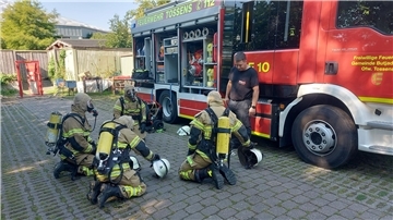 Feuerwehr in voller Montur knien vor einem Feuerwehrauto.