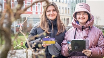 Zwei Schülerinnen halten ein Handy und ein Tablet. Auf dem Handy sind die Farben der ukrainischen Flagge zu erkennen.