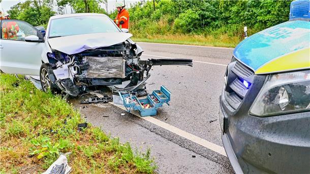 Ein verunfalltes Auto auf einer Landesstraße und ein nebenstehendes Polizeiauto.