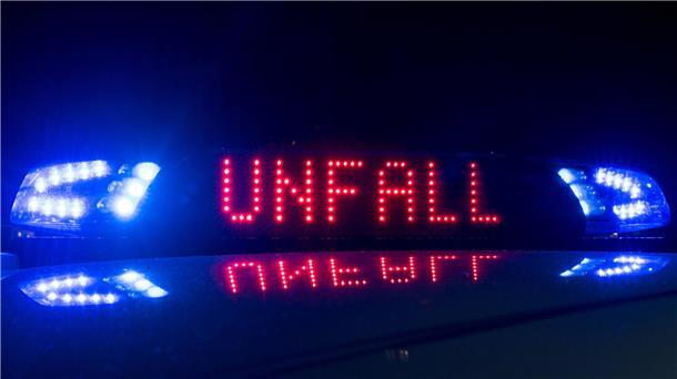 Das Blaulicht auf einem Fahrzeug der Polizei leuchtet in der Dunkelheit, während auf dem Display der Hinweis "Unfall" zu lesen ist.