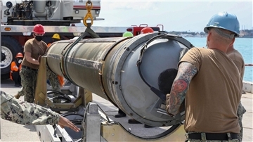 Zwei Männer bugsieren eine an einem Kran hängende Tomahawk-Rakete in die dafür vorgesehene Halterung.
