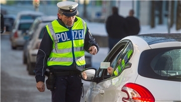 Ein Polizist in Warnweste kontrolliert einen Autofahrer. 