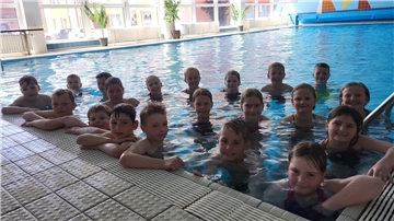 Dutzende Kinder stehen am Beckenrand eines Schwimmbeckens und lächeln in die Kamera. 