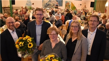 Drei Männer und eine Frau vor einer Gruppe von Menschen an Tischen.