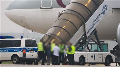 Polizisten begleiten Personen in ein Flugzeug. 