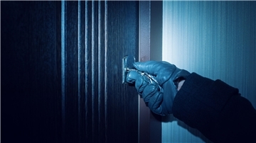 Eine vermummte Person stemmt ein Fenster auf.