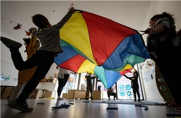 Kinder einer Kindergartengruppe nehmen in einem Gruppenraum mit ihren Erzieherinnen an einer Bewegungseinheit teil
