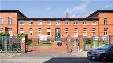 rotes Backsteingebäude mit grüner Tür in einer parkähnlichen Anlage 