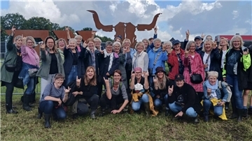 Viele Frauen stehen und hocken in zwei Reihen vor einem großen Rinderschädel aus Metall.