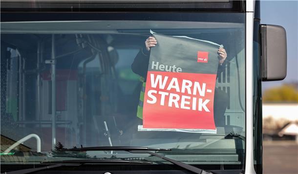 Mensch klebt ein weiß-rotes Plakat an die Windschutzscheibe eines Busses.