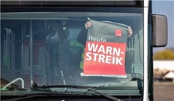 Mensch klebt ein weiß-rotes Plakat an die Windschutzscheibe eines Busses.