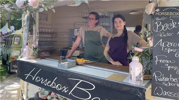 Diese beiden Damen servieren Getränke aus einem umgebaute alten Pferdeanhänger - der Horsebox Bar.