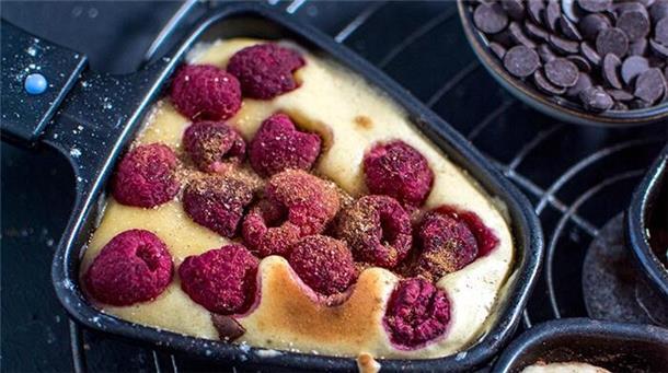 Raclette-Pfännchen mit Pfannkuchen-Teig und Himbeeren.