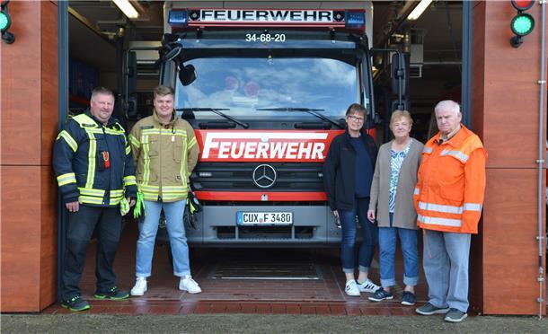 Fünf Menschen stehen vor einem Feuerwehrauto.