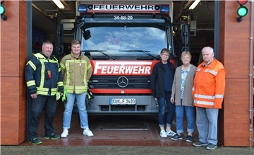 Fünf Menschen stehen vor einem Feuerwehrauto.