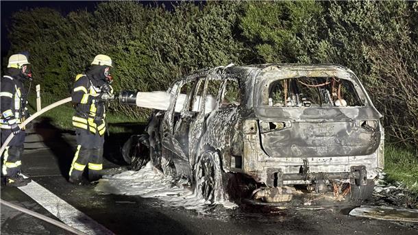 Feuer zerstört Wagen auf der Autobahn bei Sittensen komplett Zwei Feuerwehrleute stehen neben einem ausgebrannten Auto und besprühen es mit Löschschaum.