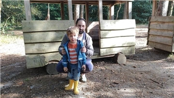 Abenteuer für Kinder auf Zevens größtem Spielplatz Ein Mann hockt hinter einem kleinen Jungen in gelben Gummistiefeln.