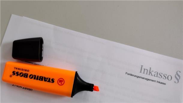 Ein orangefarbener Textmarker liegt geöffnet auf einem Brief, auf dem Inkasso zu lesen ist.