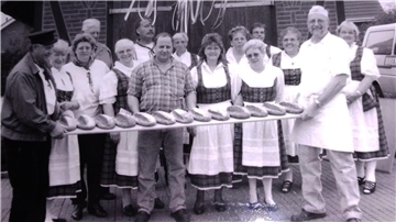 Mehrere Menschen halten ein langes Brett mit frischen Backwaren in die Höhe.